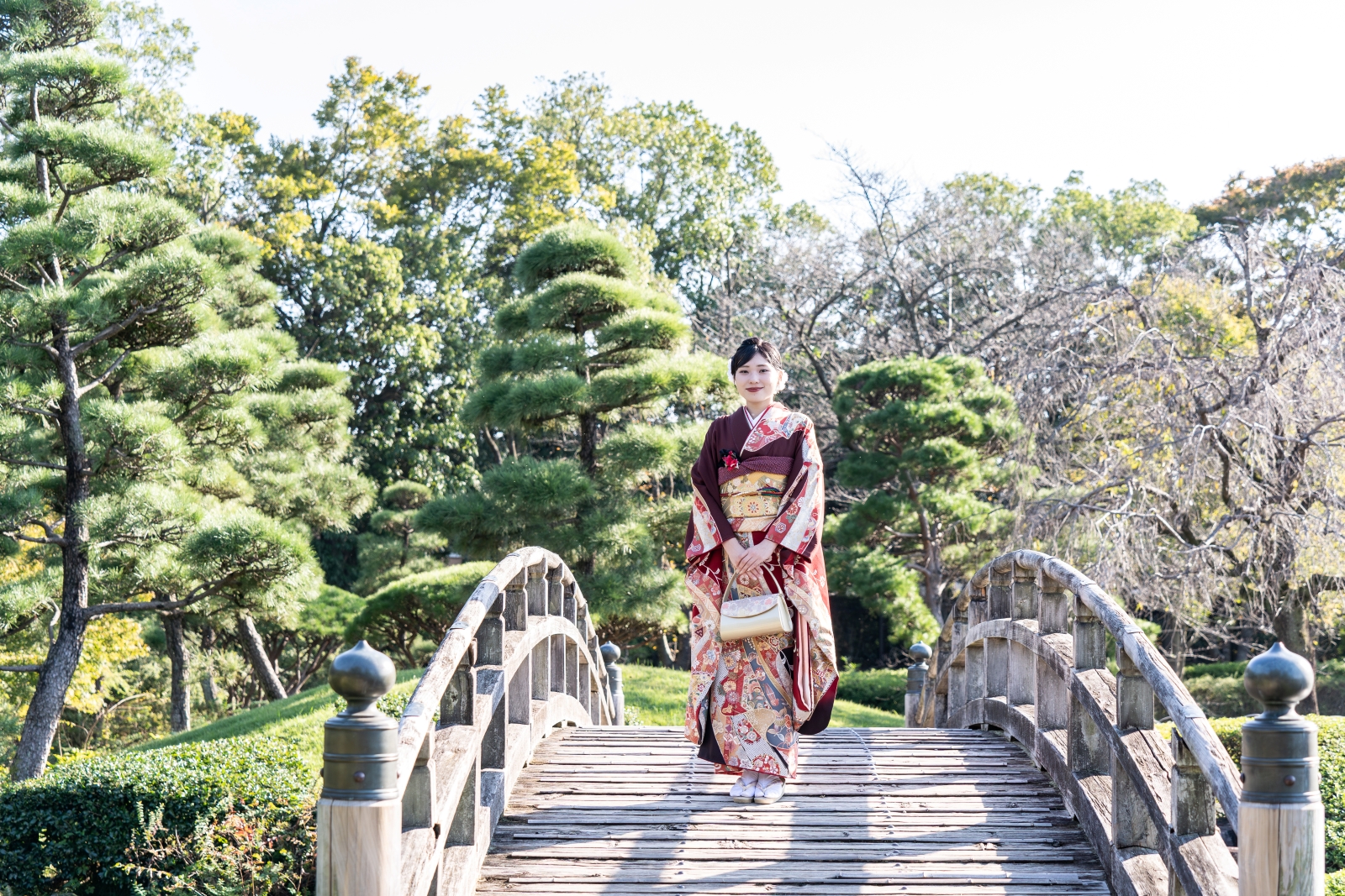 日本庭園・花田苑の太鼓橋の真ん中に立つ、美しい振袖姿の女性の全身写真。晴れの日、成人式撮影のロケーション風景