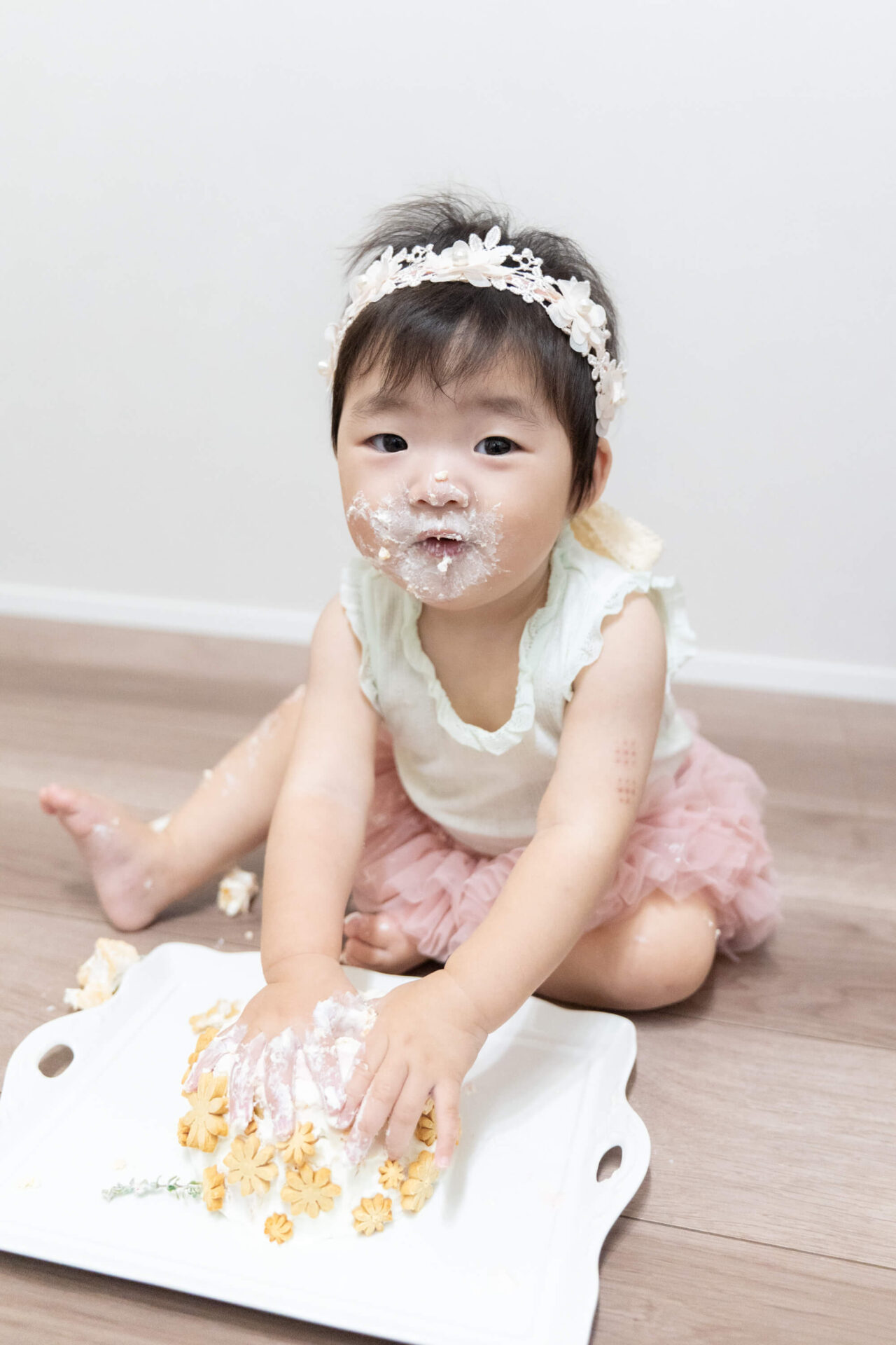 越谷市のイロドリフォトのおうちスタジオで1歳の誕生日を祝うスマッシュケーキ撮影。顔や手にクリームをいっぱいつけてケーキを食べる女の子